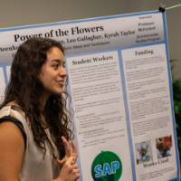 A student smiles while speaking to guests about her poster regarding flowers